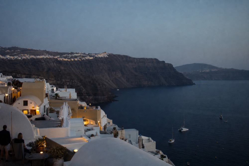 A hard shadow line creeping up a volcanic cliff face as the sun drops, the water below already in deep shade