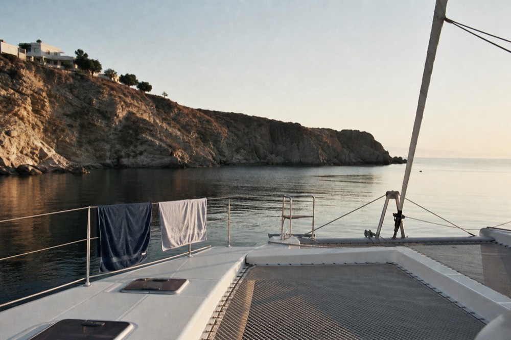 An almost empty catamaran deck in soft late-season light, two towels drying on the guardrail and long shadows across the trampoline