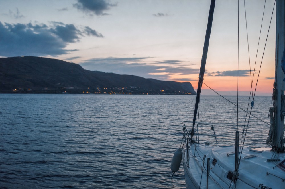 Blue-hour water with the last apricot band on the horizon and the first lights showing on a distant dark headland