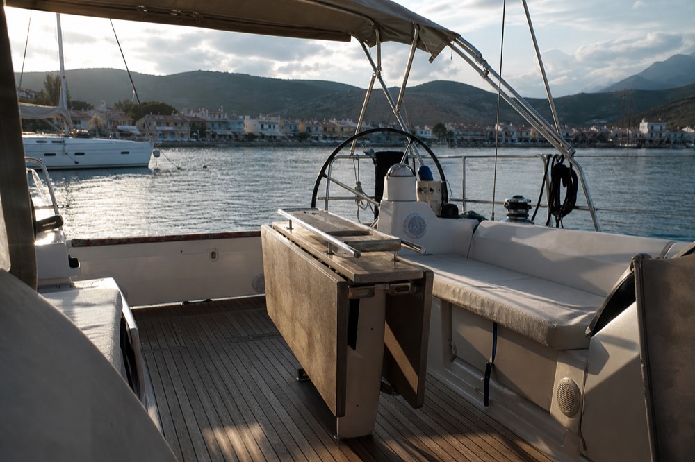 An empty teak cockpit with pale cushions and a folded chart table, low sun throwing long shadows across the deck boards