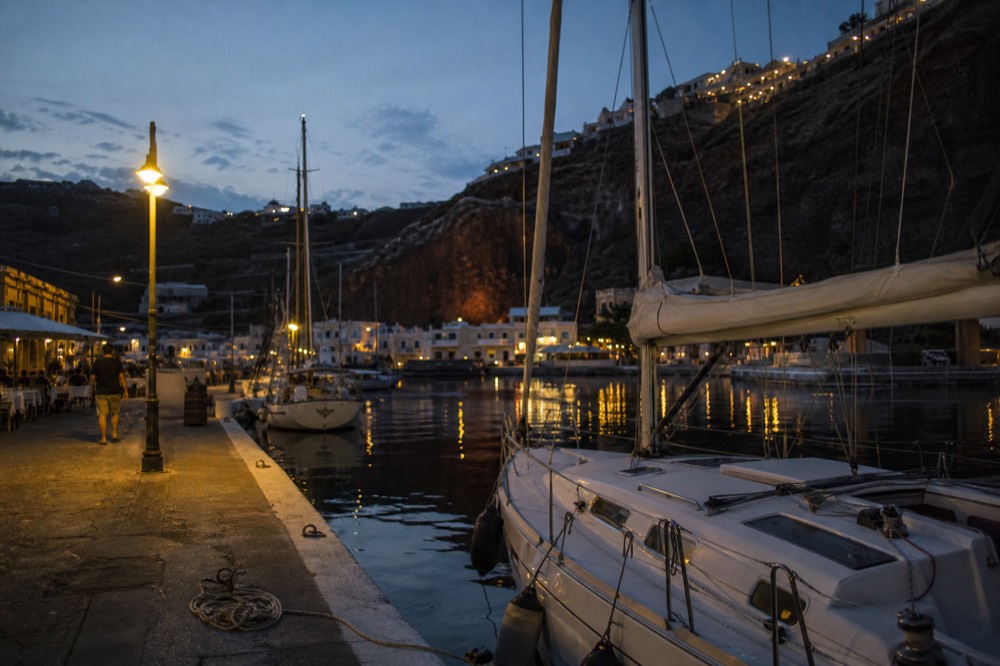A narrow marina channel at dusk with mooring lines coiled on a concrete quay and warm lamplight spilling across still black water