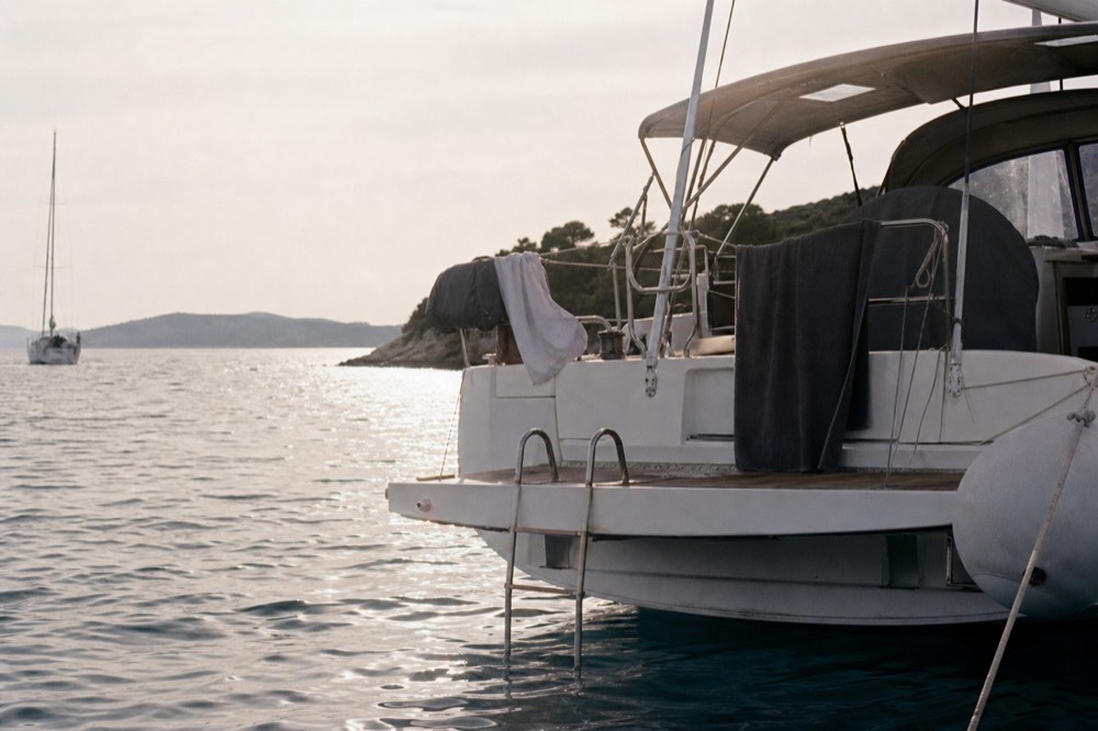 A swim platform and boarding ladder at the stern of an anchored yacht, towels drying on the rail, evening light flat on the water