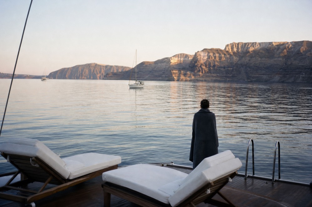 Empty sun loungers and a quiet swim platform on a boat's stern with the low volcanic island dark in the background